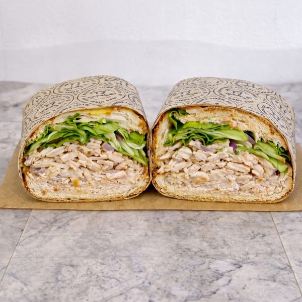 Two halves of a chicken salad sub sandwich, wrapped in paper, on a marble surface.