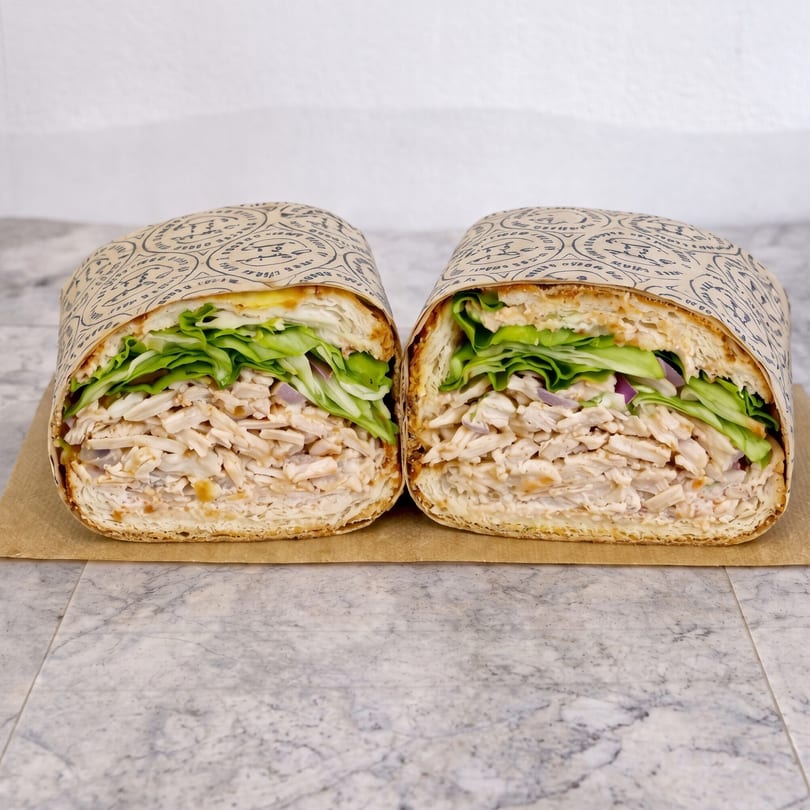 Two halves of a chicken salad sub sandwich, wrapped in paper, on a marble surface.